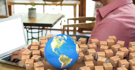 globe and multiple delivery boxes against mid section of a person using laptop in a cafe