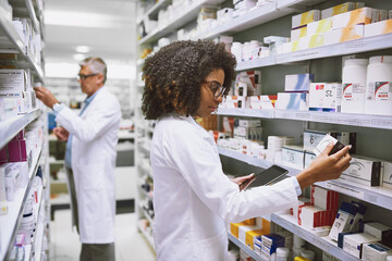 Poster - More hands equals less work. Shot of two focused pharmacist walking around and doing stock inside of a pharmacy.