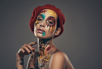 Serving all kinds of attitude. Studio shot of a young woman posing with paint on her face on a grey background.