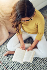 Poster - Reading widens my expertise as a wordsmith. Shot of a young woman reading a book while relaxing at home.