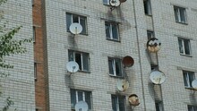 A High-rise Apartment Building Made Of White Brick With A Lot Of Old Rusty Satellite Dishes On The Windows.