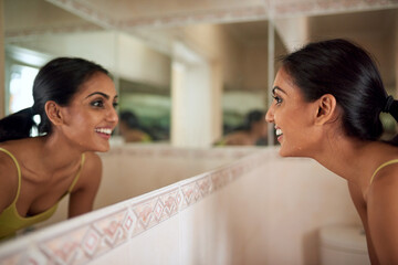 Keeping her skin looking healthier and revitalised. Cropped shot of a young woman looking at her face in the bathroom mirror.