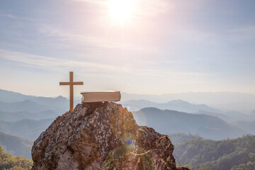 crucifix symbol and bible on top mountain with bright sunbeam on the colorful sky background