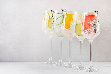 Gin and tonic cocktails set. Trendy Alcoholic drinks with lime, lemon, grapefruit, orange, cucumber, soda and spicy herbs in wine glasses, gray background. Summer cocktail party