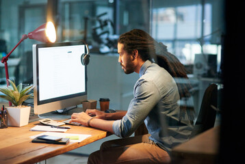 Fototapete - Working for success while others dream of it. Cropped shot of a young designer working late on a computer in an office.