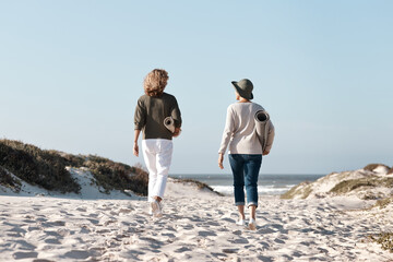 Wall Mural - Heading out to find the perfect spot. Rearview shot of two unrecognizable woman walking with their mats on the beach.