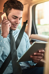 Canvas Print - Managing business on the go. Shot of a young businessman talking on a phone while using a digital tablet in the back seat of a car.