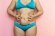 Massage woman sagging belly with hands closeup, folds on stomach, loose skin and cellulite. Naked overweight plus size girl on pink background in blue underwear. Concept of dieting and body control.
