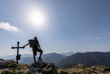 Germany, Bavaria, Sun Shining Over Silhouette Of Male Hiker Standing By Fockenstein Summit Cross