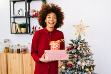 Happy Woman With Gifts Standing By Christmas Tree At Home