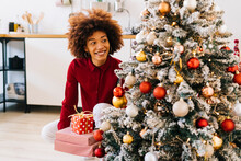 Happy Woman With Gifts Sitting By Christmas Tree At Home