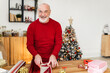 © Westend61 - Cheerful senior man wrapping Christmas presents on table at home