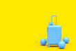 Suitcase with beach ball and flip flops on monochrome yellow background.