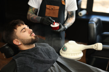 Wall Mural - Professional hairdresser with shaving foam near bearded client in barbershop