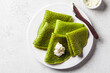 Spinach crepes on white plate, top view. Green pancakes with cream cheese, gray background, copy space.
