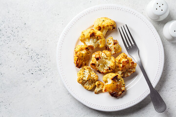 Wall Mural - Baked crispy spicy cauliflower on white plate. Cooking healthy food concept.