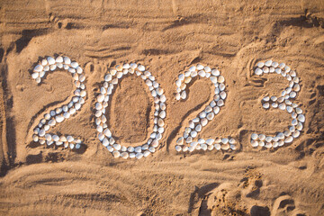 text 2023 from shells on sand by beach of sea