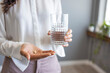 © Dragana Gordic - Close up photo of one round white pill in young female hand. Woman takes medicines with glass of water. Daily norm of vitamins, effective drugs, modern pharmacy for body and mental health concept