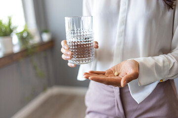 Close up woman holding pill in hand with water. Female going to take tablet from headache, painkiller, medication drinking clear water from glass. Healthcare, medicine, treatment, therapy concept