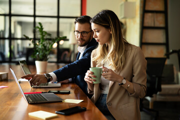 Wall Mural - Colleagues drinking coffee in office. Businesswoman and businessman discussing work in office.