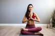 © Dragana Gordic - An Asian sports woman practices yoga in her home bedroom after waking up, sits on the living room floor in her house, meditates, exercises in sportswear.