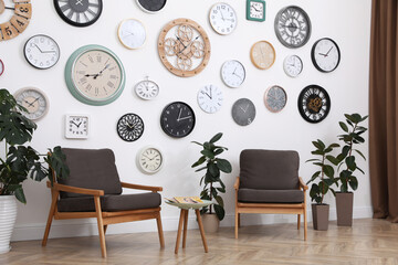 Canvas Print - Comfortable furniture, beautiful houseplants and collection of different clocks on white wall in room