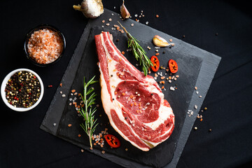 raw meat on a black board with chili, papper, garlic and rosemary