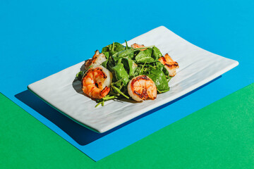 Wall Mural - Salad with shrimps and arugula on white dish on colored background