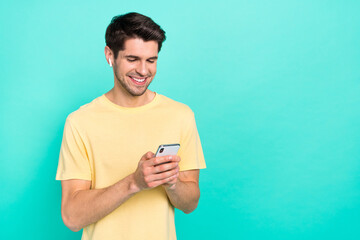 Photo of funny brunet young guy listen music look telephone wear t-shirt headphones isolated on teal color background