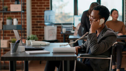 Wall Mural - Company employee answering landline phone call in office, dealing with physical disability. Businessman using telephone to talk to people, having conversation about financial marketing.