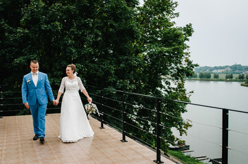 Wall Mural - The bride and groom walk on wedding ceremony on pier. A newlyweds couple walking in a country. Photo near lake outdoors.