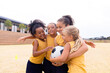 Cheerful multiracial elementary schoolgirls with soccer ball embracing while standing on ground