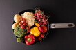 Overhead view of various colorful vegetables in frying pan on black background