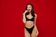© ViDi Studio - Young sexy hot brunette woman 20s with perfect fit body wear black underwear look aside biting nails fingers touch lips isolated on plain red background studio portrait. People female beauty concept