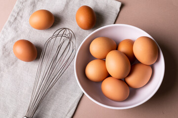 Directly above view of fresh brown eggs in bowl by wire whisk on napkin over table