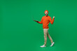 Full body young smiling happy caucasian man in orange sweatshirt hat hold use work on laptop pc computer walk go do winner gesture isolated on plain green background studio. People lifestyle concept