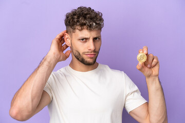 Wall Mural - Young caucasian man holding a Bitcoin isolated on purple background having doubts