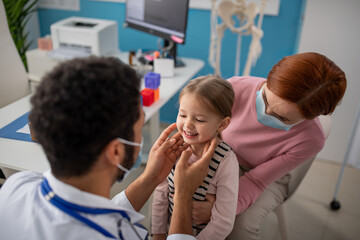 Wall Mural - young male doctor checking little girl's lymph nodes in his office.