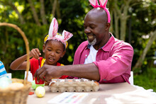 African American Girl And Grandfather Wearing Bunny Ears While Painting Eggs On Easter Day