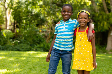 Wall Mural - Portrait of smiling african american boy and girl standing with arms around in backyard