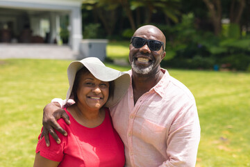 Wall Mural - Portrait of cheerful african american senior couple standing together in backyard on sunny day