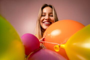 Wall Mural - Studio portrait of a happy young blonde woman with balloons over pink background.