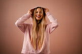 Fototapeta Nowy Jork - Fashion studio portrait of a happy young blonde woman in hoodie posing over pink background.