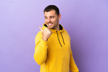 Wall Mural - Brazilian man over isolated purple background pointing to the side to present a product