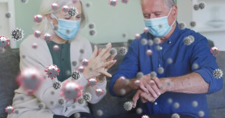 Poster - Animation of virus cells over senior caucasian couple disinfecting hands at home with face masks