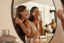 We Always Have A Joke Prepared. Shot Of Two Young Friends Standing Together And Using A Mirror To Touch Up Their Makeup At A Dinner Party.