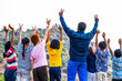 Back view shot of group of teenage kids with teacher celebrating by raising hands on top of hill after reaching destination - concept of summer holiday, trekking, outdoor adventures activities and