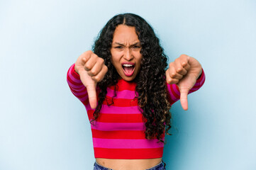 Wall Mural - Young hispanic woman isolated on blue background showing thumb down and expressing dislike.