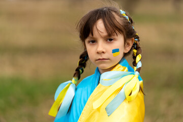 Close-up portrait of a small beautiful Ukrainian girl with two pigtails with yellow and blue ribbons like the Ukrainian flag. She asks for help to save Ukraine. Stop the war