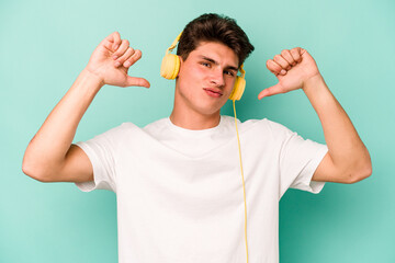 Young caucasian man listening to music isolated on blue background feels proud and self confident, example to follow.